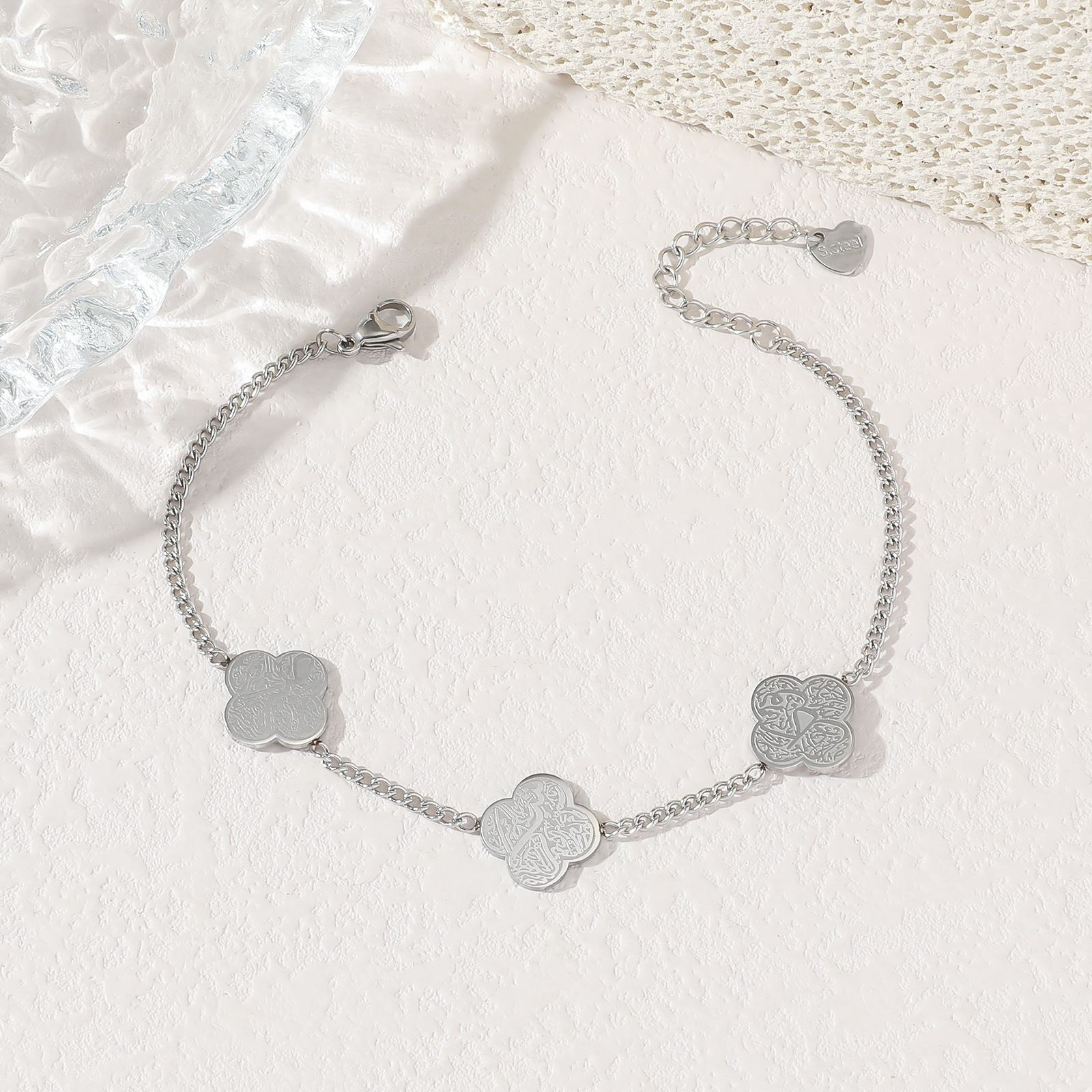 Silver four-leaf clover charm bracelet flat lay on white background