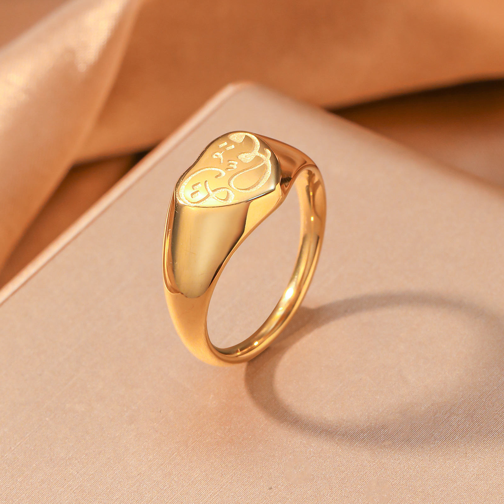 CIGAONI 18K gold Hubb Arabic love calligraphy heart signet ring angled view on beige fabric surface

