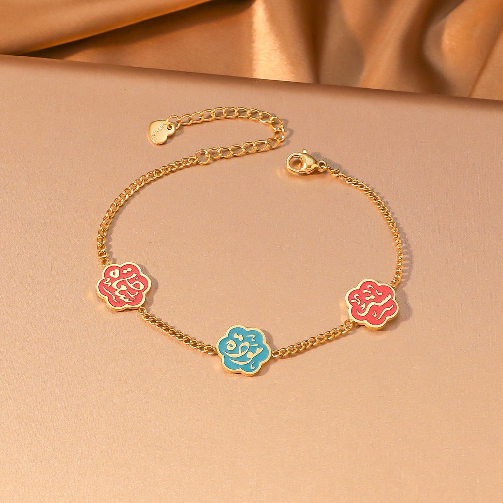 CIGAONI Floral Faith Bracelet Gold – Flat lay of gold chain bracelet with two red and one blue enamel Arabic calligraphy flower charms

