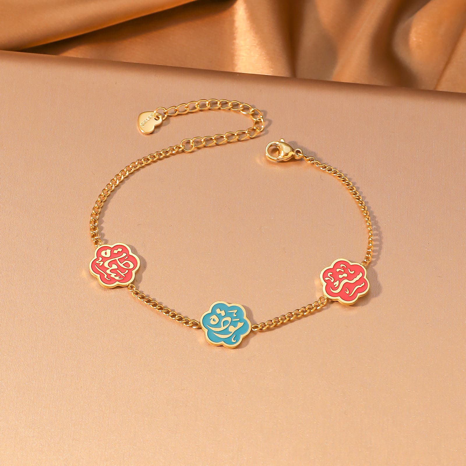CIGAONI Floral Faith Bracelet Gold – Flat lay of gold chain bracelet with two red and one blue enamel Arabic calligraphy flower charms

