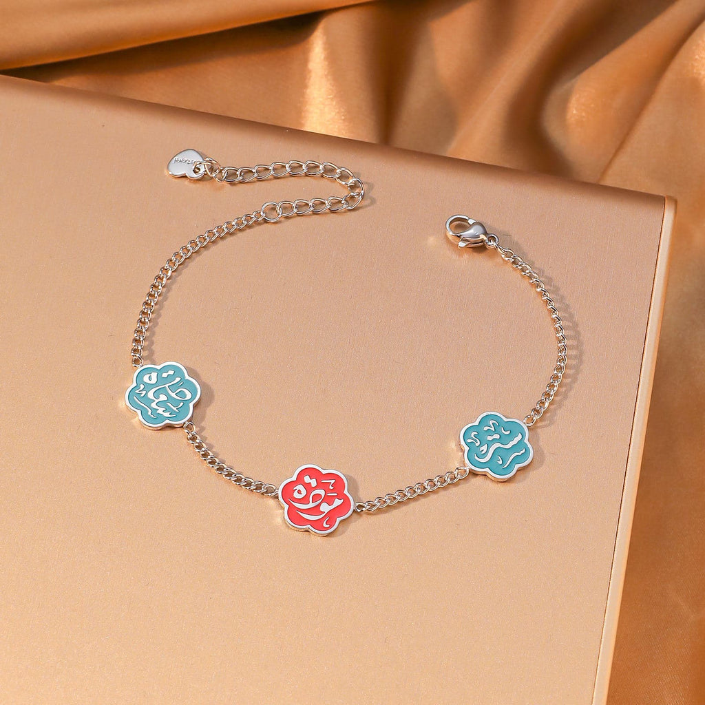 CIGAONI Floral Faith Bracelet Silver – Flat lay of silver chain bracelet with two blue and one red enamel Arabic calligraphy flower charms

