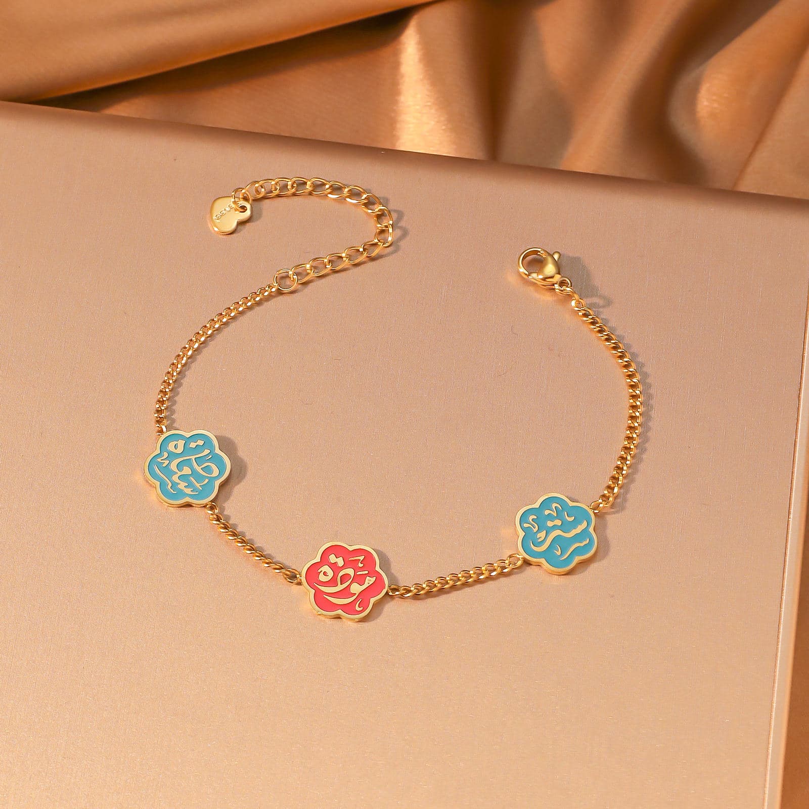 CIGAONI Floral Faith Bracelet Gold – Flat lay of gold chain bracelet with two blue and one red enamel Arabic calligraphy flower charms

