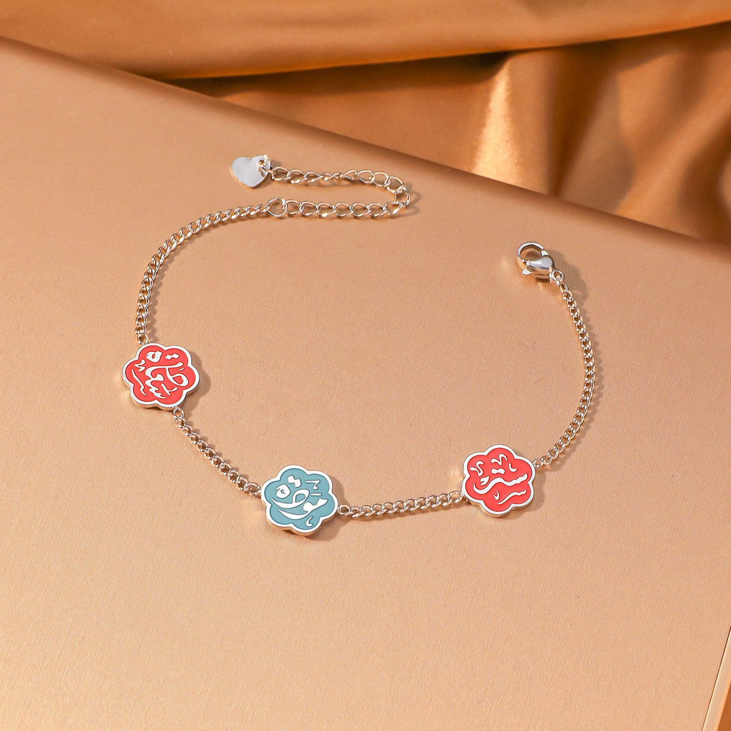 CIGAONI Floral Faith Bracelet Silver – Flat lay of silver chain bracelet with two red and one blue enamel Arabic calligraphy flower charms



