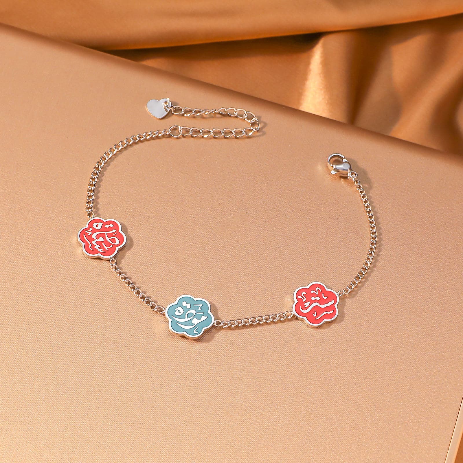 CIGAONI Floral Faith Bracelet Silver – Flat lay of silver chain bracelet with two red and one blue enamel Arabic calligraphy flower charms



