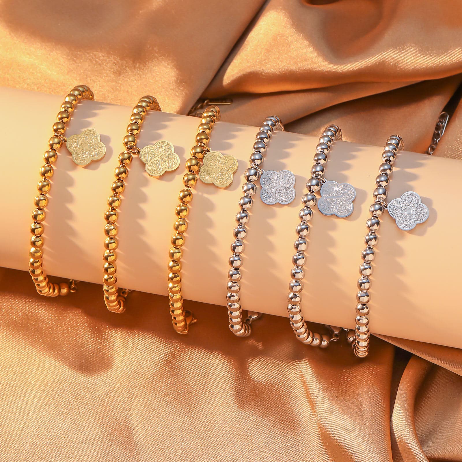 CIGAONI Clover of Virtue 18K gold bracelet on model's wrist, four-leaf quatrefoil charm engraved with Arabic calligraphy, beaded chain close-up lifestyle shot