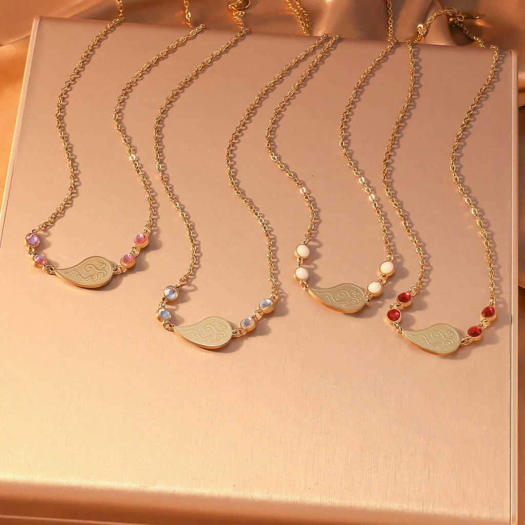 CIGAONI Dewdrop Serenity Necklace collection - engraved teardrop pendant necklaces in gold and silver with colorful zircon accents on warm background