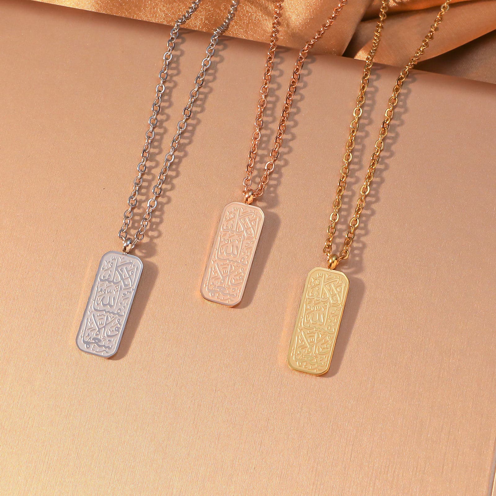 CIGAONI Allah Arabic Calligraphy Rectangular Plaque Necklace in three finishes - Silver, Rose Gold and 18K Gold - displayed side by side on beige background