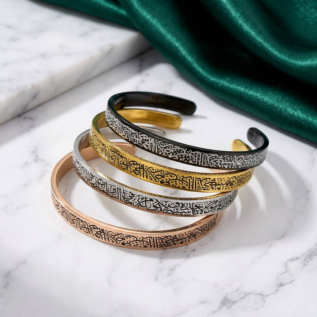CIGAONI Sacred Heritage Ayatul Kursi open cuff bangles in gold, silver, rose gold and black displayed on marble with green silk backdrop

