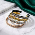 CIGAONI Sacred Heritage Ayatul Kursi open cuff bangles in gold, silver, rose gold and black displayed on marble with green silk backdrop

