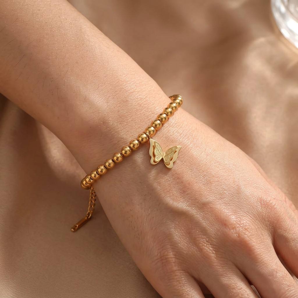  CIGAONI Wings of Amal 18K gold butterfly charm bracelet on model's wrist, beaded chain with lobster clasp extender, elegant close-up lifestyle shot

