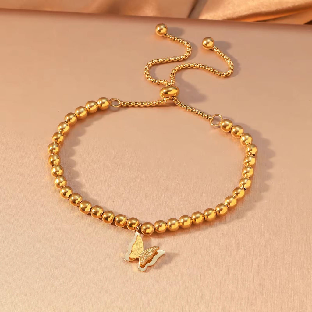 CIGAONI Wings of Amal gold butterfly bracelet with pull-out adjustable sliding clasp, beaded chain, flat lay on warm beige background

