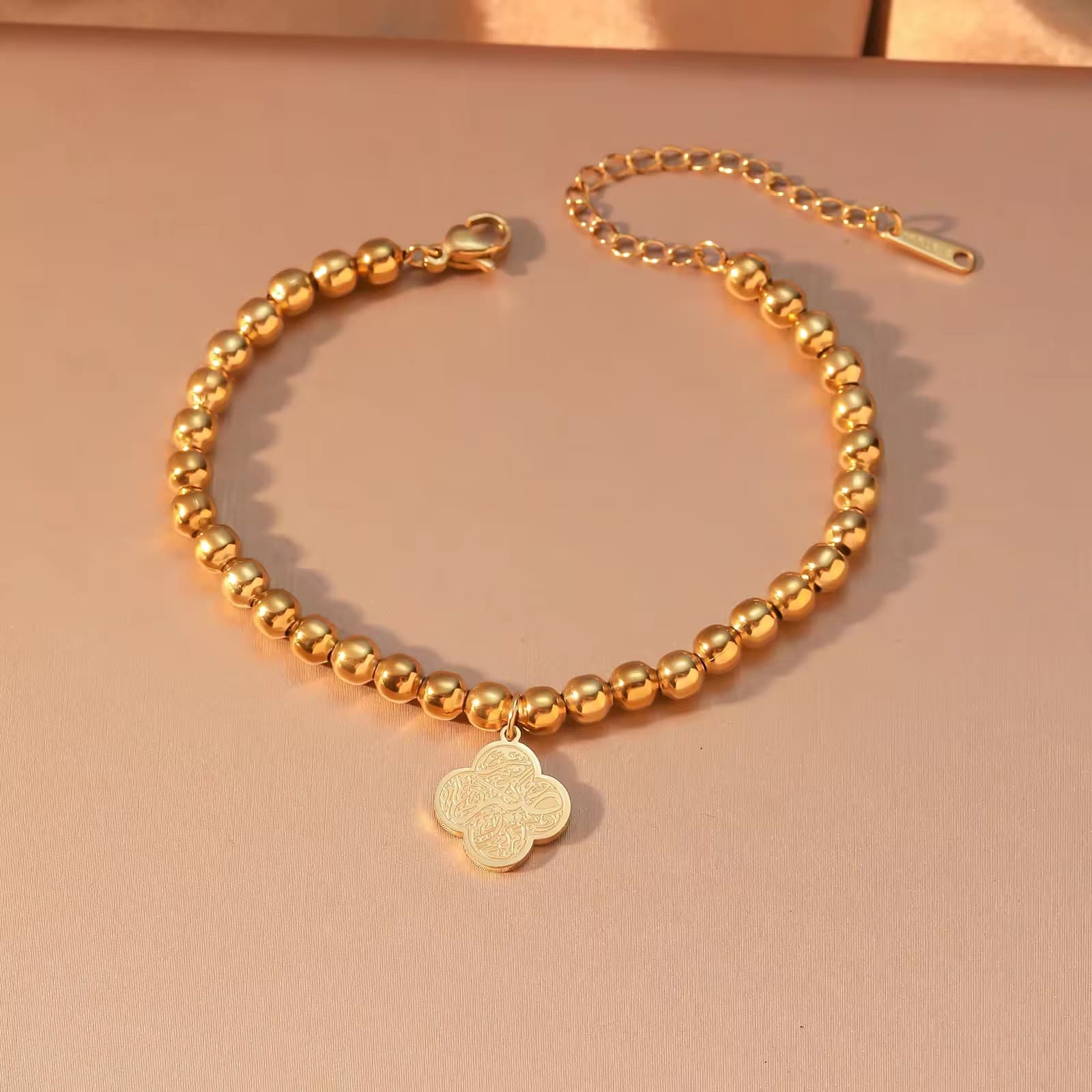 CIGAONI Clover of Virtue 18K gold beaded bracelet flat lay in warm light, quatrefoil Arabic calligraphy charm with lobster clasp, elegant spiritual jewelry