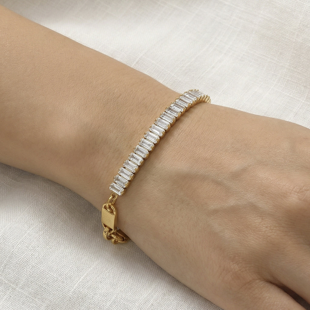 CIGAONI Pure Brilliance Gold Rectangular Tennis Bracelet – Baguette Clear Zirconia Close-up on Wrist, Gold Folding Clasp Detail, Linen Background