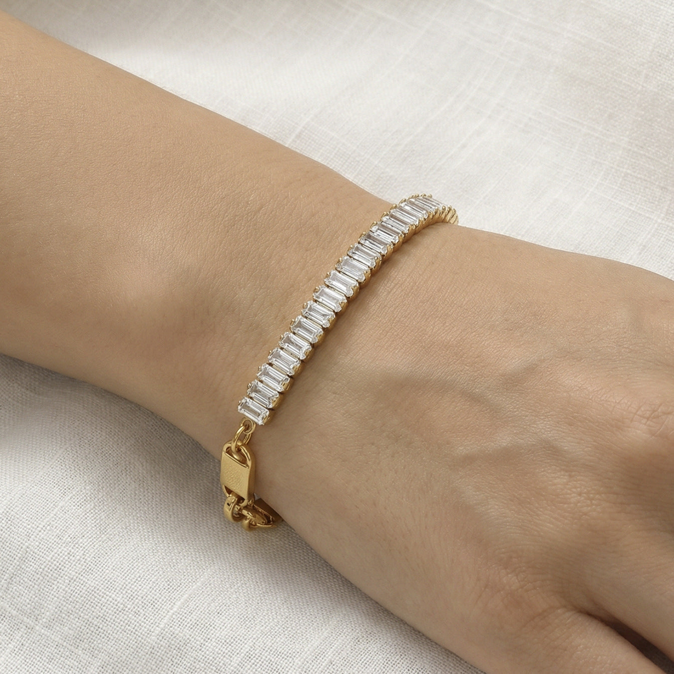 CIGAONI Pure Brilliance Gold Rectangular Tennis Bracelet – Baguette Clear Zirconia Close-up on Wrist, Gold Folding Clasp Detail, Linen Background