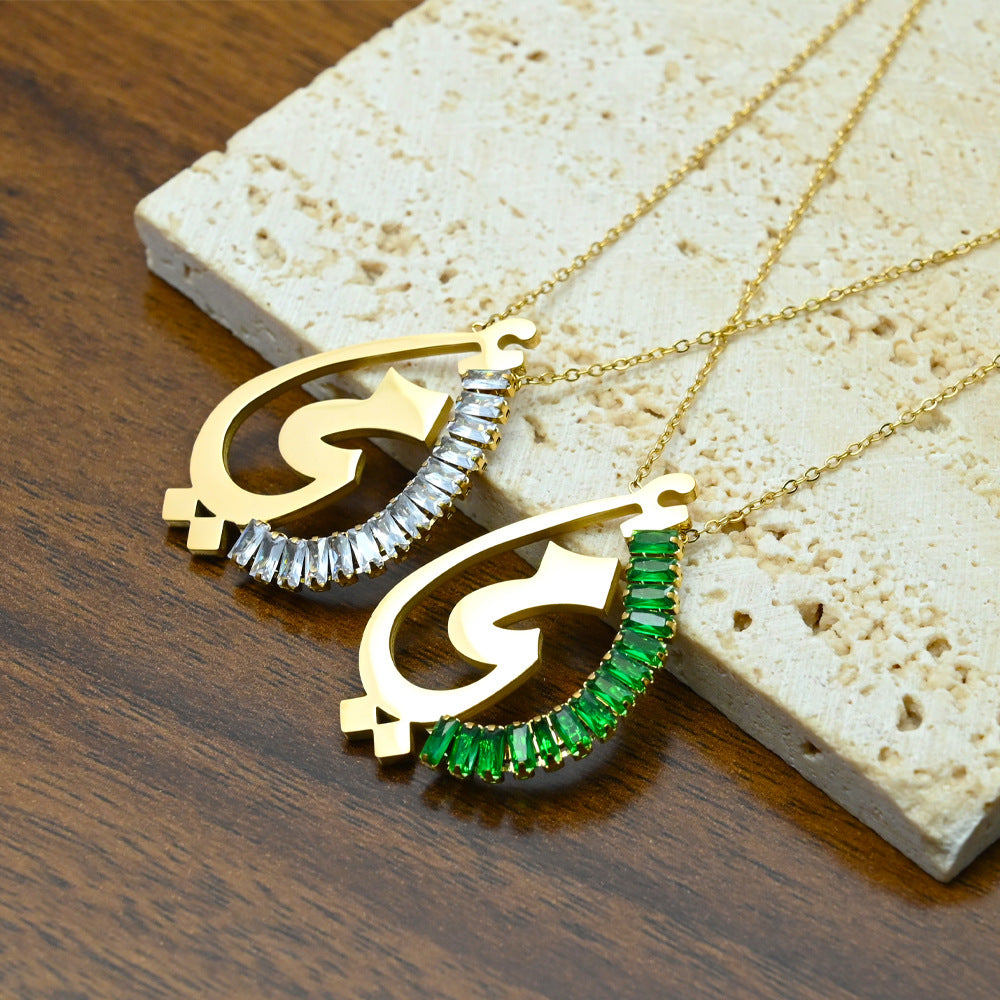 Gold Arabic calligraphy pendant necklace with green crystal embellishments, flat lay on marble surface